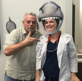 older man next to the dentist wearing a shark head mask